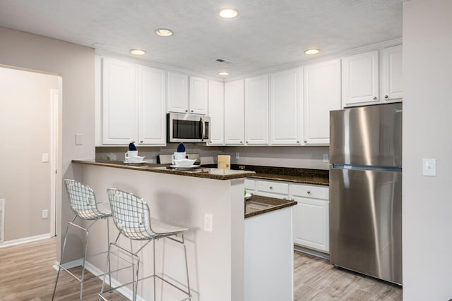 kitchen with stainless steel appliances, white cabinets, a kitchen bar, and light hardwood / wood-style flooring