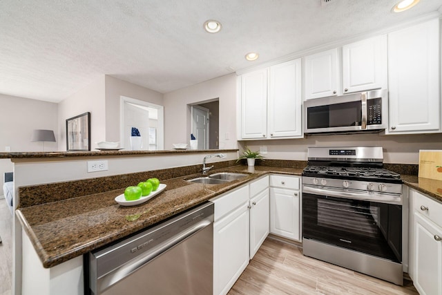 kitchen with appliances with stainless steel finishes, sink, white cabinets, dark stone counters, and kitchen peninsula