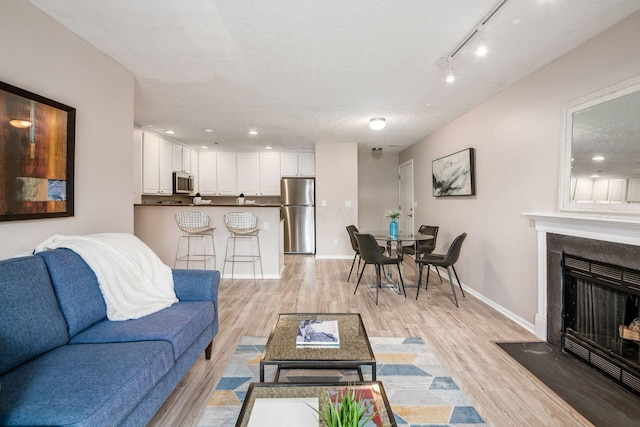 living room featuring rail lighting, light hardwood / wood-style floors, and a textured ceiling