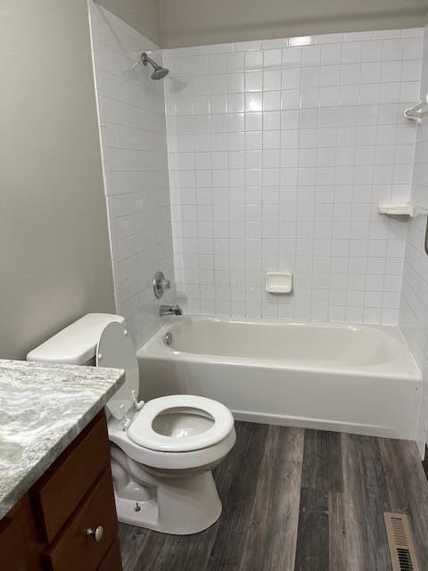 full bathroom with hardwood / wood-style flooring, vanity, tiled shower / bath, and toilet