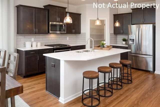 kitchen with appliances with stainless steel finishes, pendant lighting, sink, a kitchen island with sink, and light hardwood / wood-style flooring