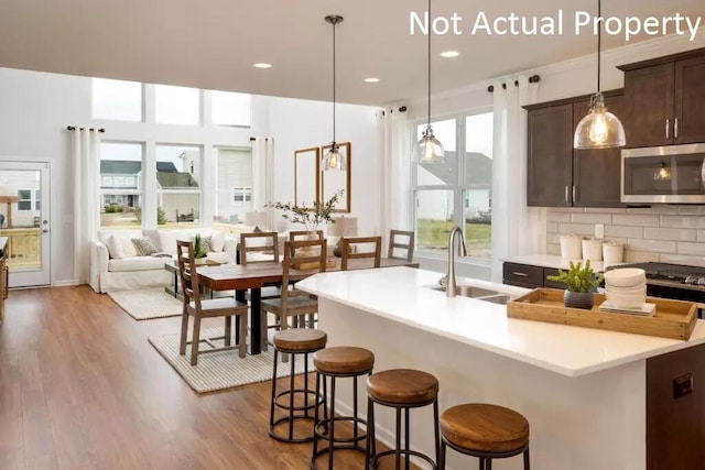 kitchen featuring sink, a kitchen island with sink, hanging light fixtures, dark brown cabinetry, and wood-type flooring