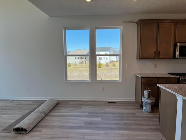 kitchen featuring light stone countertops, baseboards, light wood finished floors, black gas stove, and stainless steel microwave