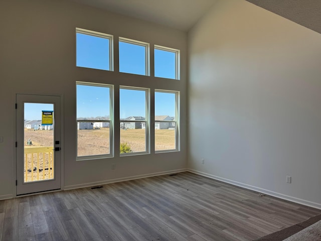 unfurnished room with visible vents, baseboards, high vaulted ceiling, and wood finished floors