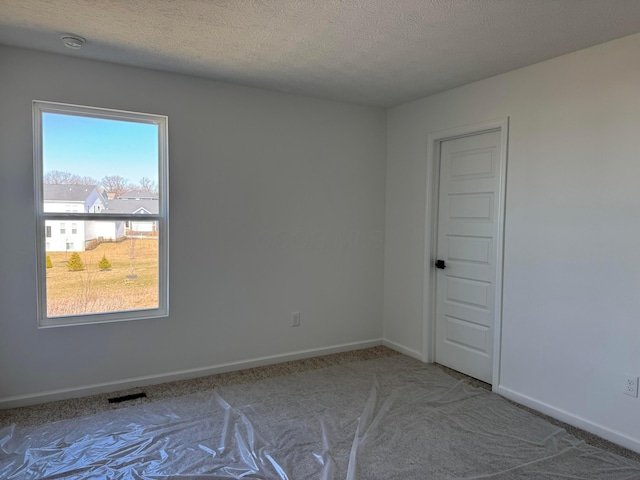 carpeted spare room with visible vents, baseboards, and a textured ceiling