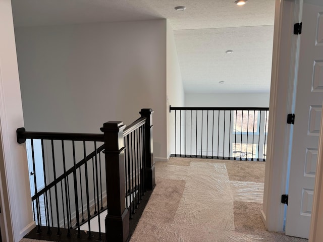 hallway featuring an upstairs landing, carpet flooring, a textured ceiling, and baseboards