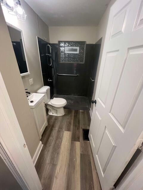 bathroom with hardwood / wood-style flooring, tiled shower, vanity, and toilet