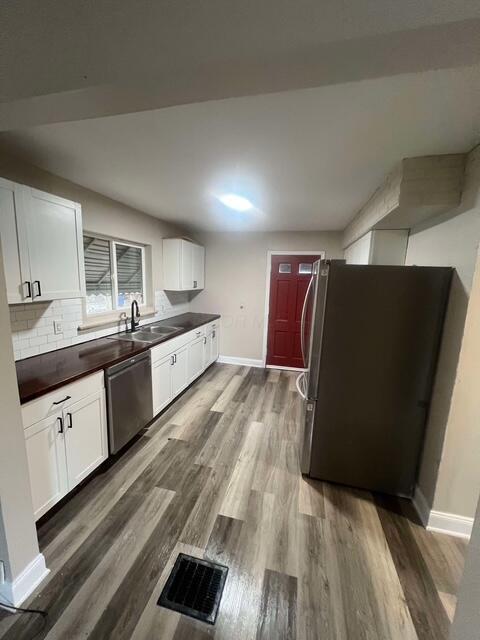 kitchen with sink, dark wood-type flooring, white cabinetry, stainless steel appliances, and tasteful backsplash