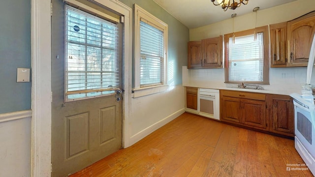 kitchen featuring white electric stove, decorative backsplash, light wood-type flooring, and a wealth of natural light