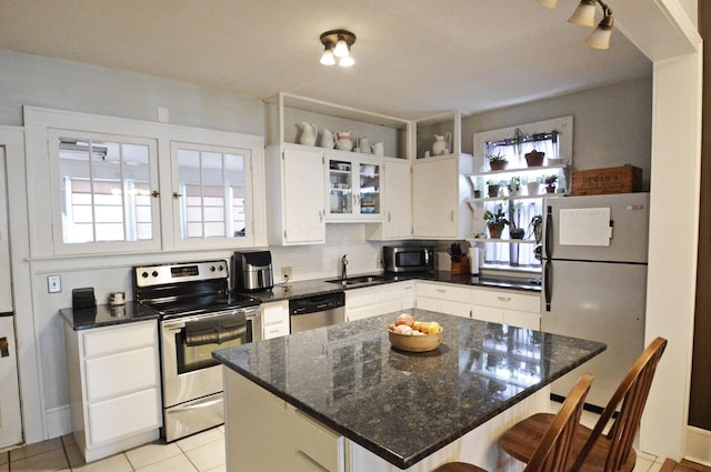 kitchen with light tile patterned flooring, a kitchen island, white cabinetry, sink, and stainless steel appliances