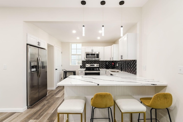 kitchen with appliances with stainless steel finishes, white cabinetry, decorative backsplash, hanging light fixtures, and kitchen peninsula