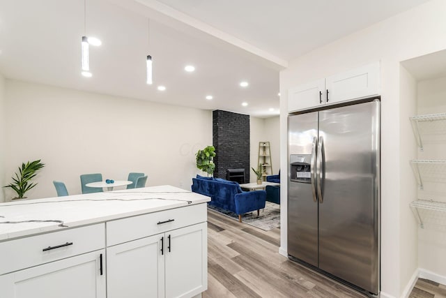 kitchen with stainless steel refrigerator with ice dispenser, white cabinetry, light stone counters, hanging light fixtures, and light hardwood / wood-style flooring