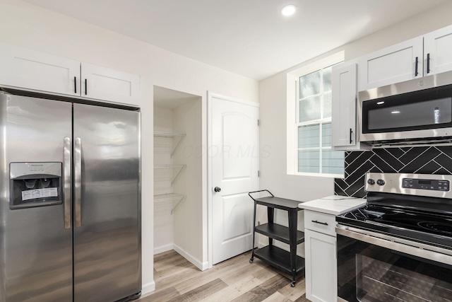 kitchen with stainless steel appliances, tasteful backsplash, white cabinets, and light hardwood / wood-style floors