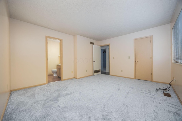 unfurnished bedroom with light carpet, a textured ceiling, and ensuite bath