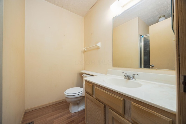 bathroom with toilet, a shower with shower door, a textured ceiling, vanity, and hardwood / wood-style flooring