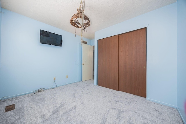 unfurnished bedroom featuring an inviting chandelier, a closet, light colored carpet, and a textured ceiling