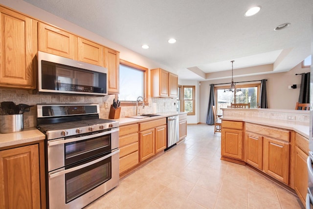 kitchen with appliances with stainless steel finishes, pendant lighting, sink, decorative backsplash, and a raised ceiling