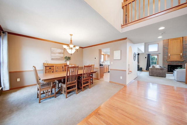 carpeted dining room featuring crown molding, a chandelier, a brick fireplace, and a high ceiling