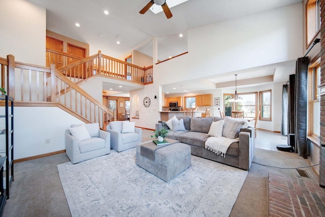 living room with a high ceiling, ceiling fan with notable chandelier, and light colored carpet