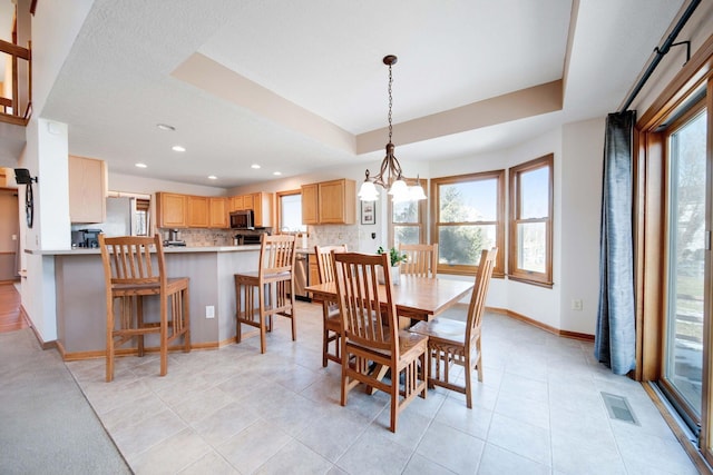 dining area with light tile patterned flooring, a healthy amount of sunlight, and a tray ceiling