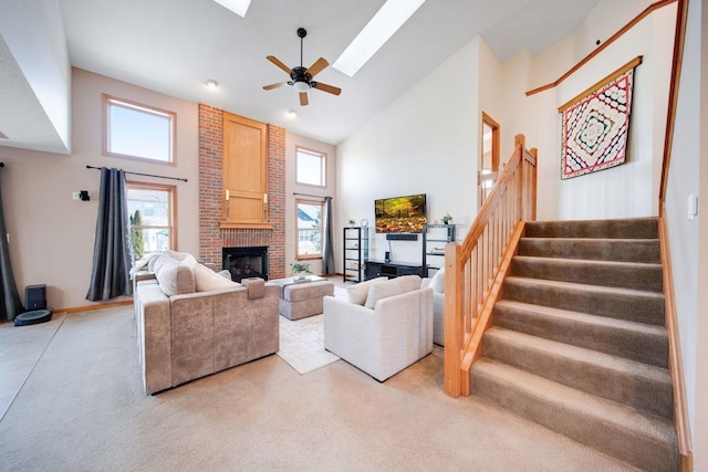 carpeted living room with ceiling fan, a skylight, high vaulted ceiling, and a brick fireplace