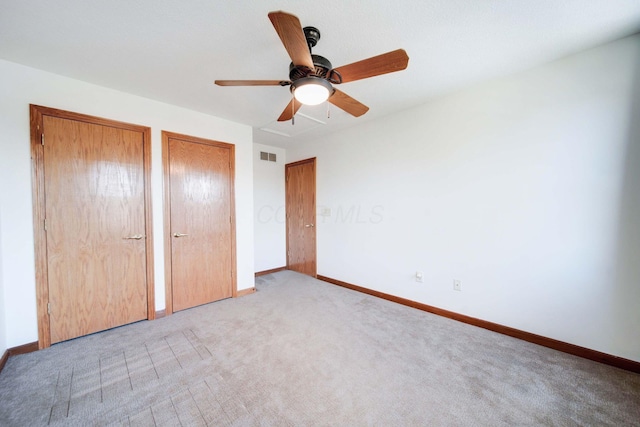 unfurnished bedroom featuring multiple closets, light colored carpet, and ceiling fan