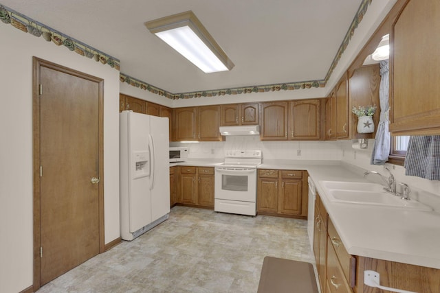 kitchen with white appliances, brown cabinetry, a sink, light countertops, and under cabinet range hood