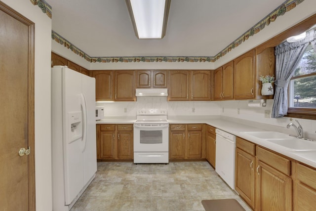 kitchen featuring brown cabinets, under cabinet range hood, a sink, white appliances, and light countertops