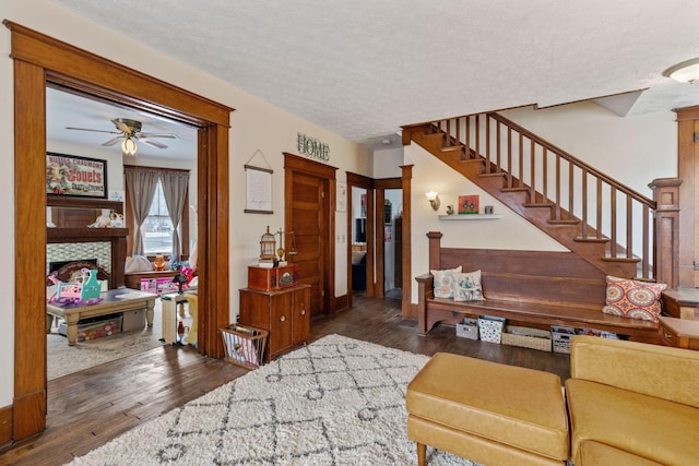 living room featuring ceiling fan, a tile fireplace, dark hardwood / wood-style floors, and a textured ceiling