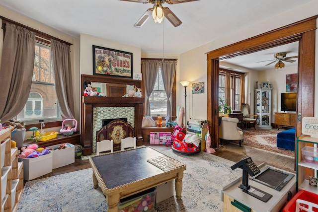 rec room featuring a tiled fireplace, plenty of natural light, hardwood / wood-style floors, and ceiling fan