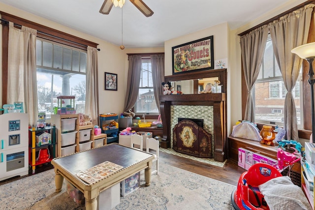 interior space with a tile fireplace, wood-type flooring, and ceiling fan