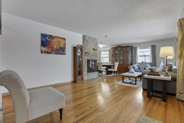 living room with a stone fireplace, light hardwood / wood-style flooring, and a textured ceiling