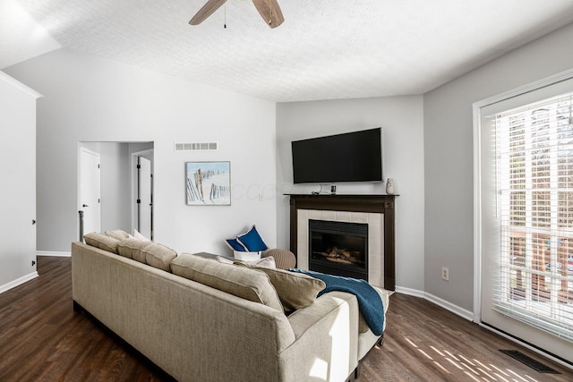 living room featuring lofted ceiling, dark hardwood / wood-style floors, a tiled fireplace, and a textured ceiling