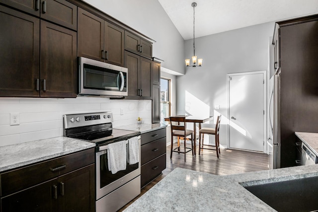 kitchen featuring appliances with stainless steel finishes, pendant lighting, decorative backsplash, light stone countertops, and dark wood-type flooring