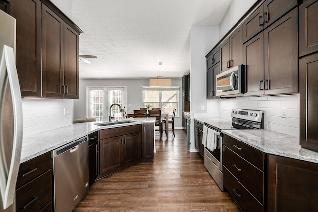 kitchen featuring pendant lighting, sink, appliances with stainless steel finishes, light stone countertops, and dark hardwood / wood-style flooring