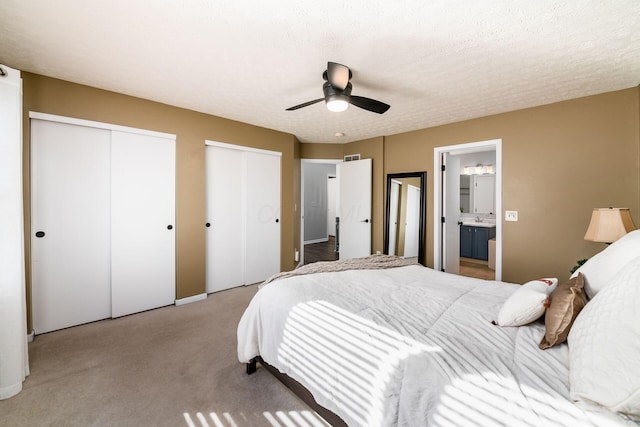 carpeted bedroom with connected bathroom, a textured ceiling, multiple closets, and ceiling fan