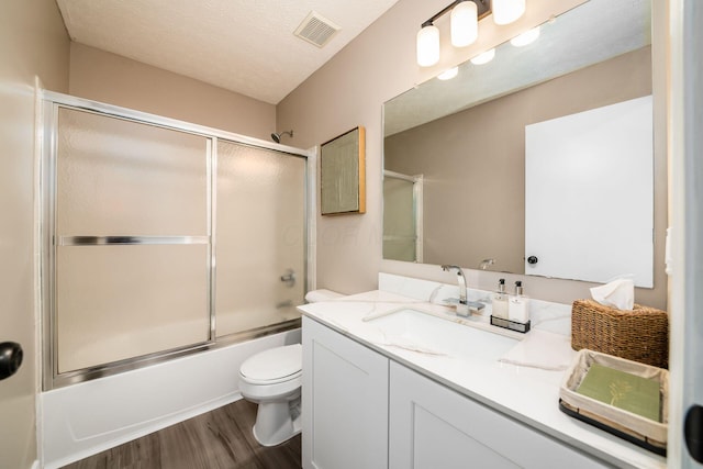 full bathroom featuring hardwood / wood-style flooring, enclosed tub / shower combo, vanity, toilet, and a textured ceiling