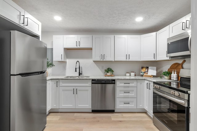 kitchen with appliances with stainless steel finishes, white cabinetry, sink, light hardwood / wood-style floors, and a textured ceiling