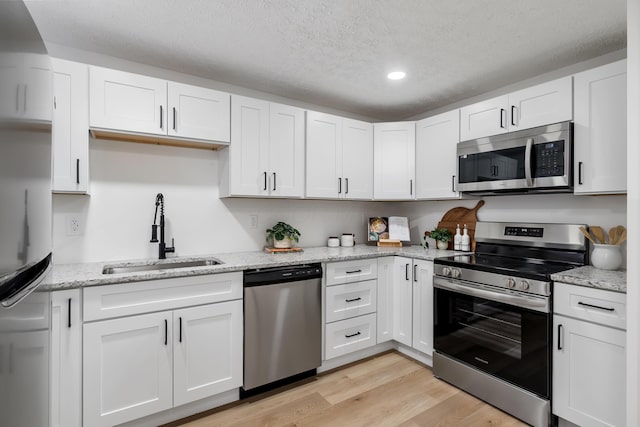 kitchen featuring sink, appliances with stainless steel finishes, white cabinetry, a textured ceiling, and light wood-type flooring