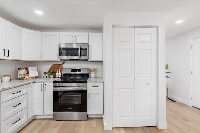 kitchen with white cabinetry, light stone countertops, light hardwood / wood-style flooring, and stainless steel appliances