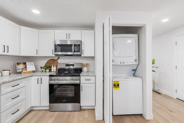 kitchen featuring stacked washer and dryer, white cabinetry, appliances with stainless steel finishes, and light wood-type flooring