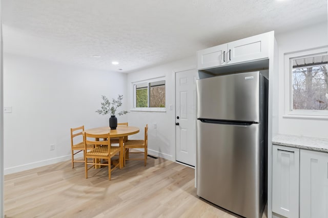 kitchen featuring stainless steel refrigerator, white cabinetry, light stone counters, a textured ceiling, and light wood-type flooring