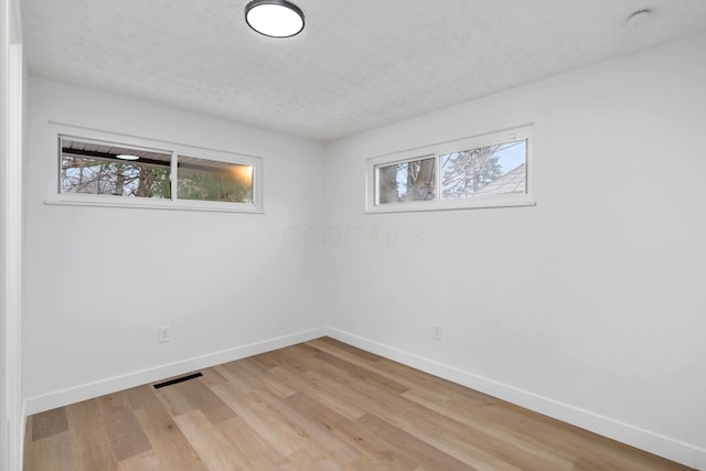 spare room with a textured ceiling, light hardwood / wood-style flooring, and a wealth of natural light