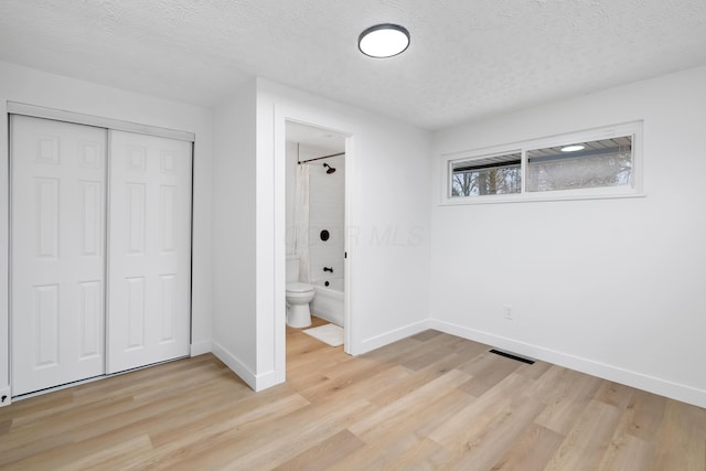 unfurnished bedroom featuring light hardwood / wood-style flooring, a closet, a textured ceiling, and ensuite bathroom