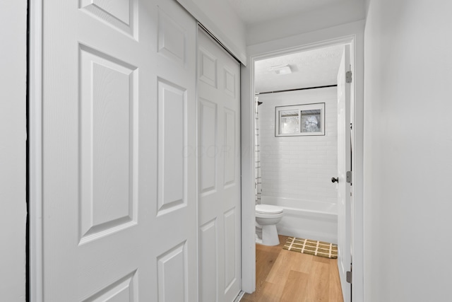 bathroom with hardwood / wood-style flooring, shower / bath combination, and toilet