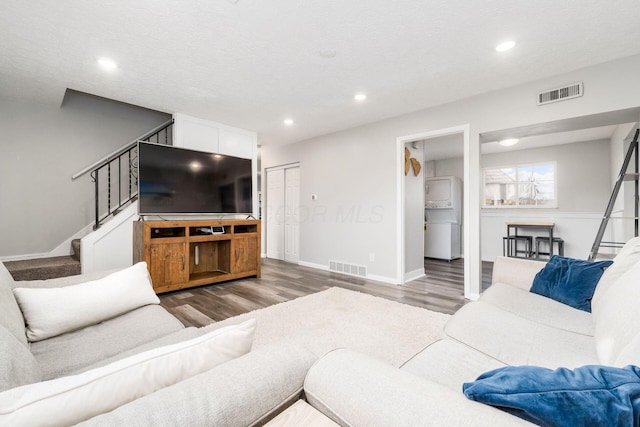 living room featuring stacked washer and clothes dryer, wood-type flooring, and a textured ceiling