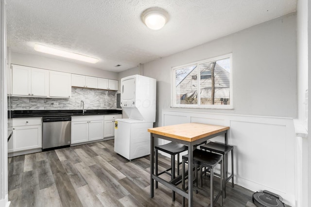 kitchen with dishwasher, wood-type flooring, sink, white cabinets, and stacked washer / drying machine