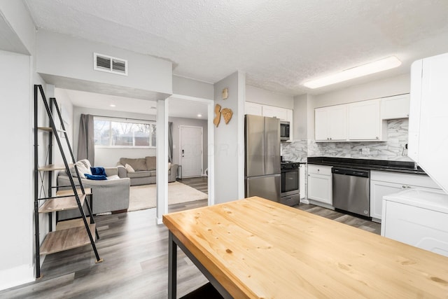 kitchen with hardwood / wood-style flooring, backsplash, stainless steel appliances, white cabinets, and a textured ceiling