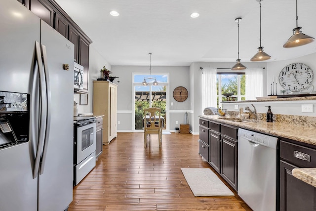 kitchen with sink, hanging light fixtures, dark brown cabinets, stainless steel appliances, and light stone counters