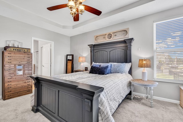 bedroom with ceiling fan, a tray ceiling, and light carpet